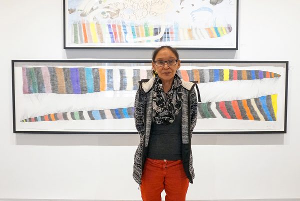Photo of Shuvinai Ashoona in a gallery in front of two of her works on paper